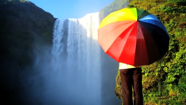 Concetto colpo di femmina solitaria da una cascata con ombrello arcobaleno — Video Stock