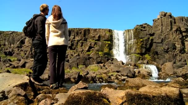 Casal jovem atlético caminhando sozinho em terreno acidentado para a cachoeira Pingvellir, Islândia — Vídeo de Stock