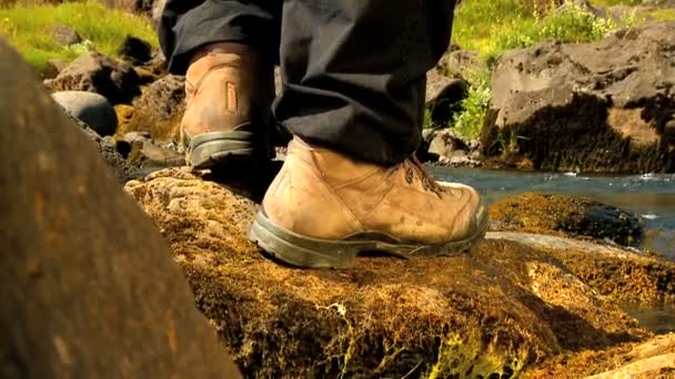 Feet of athletic hiker walking beside a glacial river — Stock Video