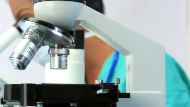Γυναίκα ερευνητής με μάσκα στο αναζητούν μέσα από ένα μικροσκόπιο — Αρχείο Βίντεο