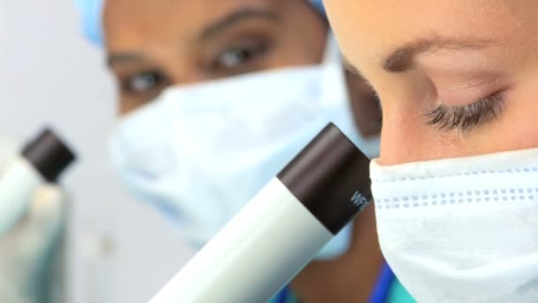 Close up de pesquisadores do sexo feminino com máscara sobre com um microscópio — Vídeo de Stock