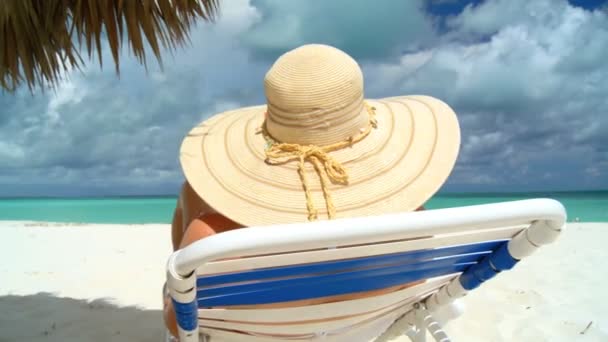 Елегантна молода жінка відпочиває на білому піщаному пляжі, дивлячись на аквамаринні води — стокове відео