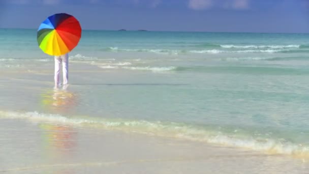 Heitere junge Frau mit einem Sonnenschirm in Regenbogenfarben an einem schönen weißen Sandstrand — Stockvideo