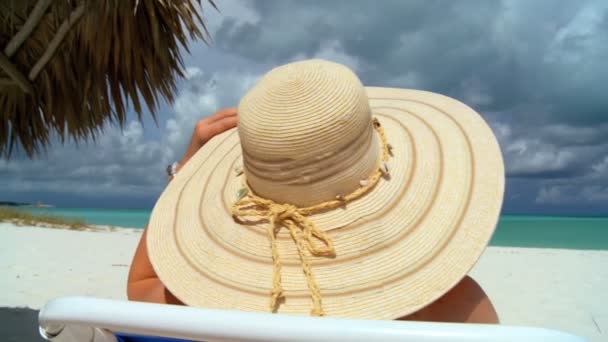 Елегантна молода жінка відпочиває на білому піщаному пляжі, дивлячись на аквамаринні води — стокове відео