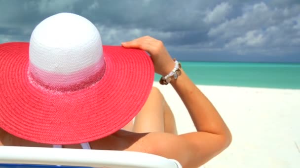 Elegante joven hembra relajándose en la playa de arena blanca mirando las aguas aguamarinas — Vídeo de stock