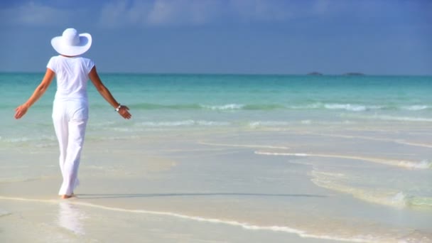 Elegante joven hembra caminando en una hermosa playa de arena blanca mirando aguas aguamarinas — Vídeos de Stock