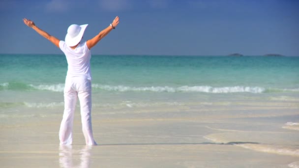 Элегантная молодая женщина празднует на красивом белом песчаном пляже, глядя на аквамариновые воды — стоковое видео