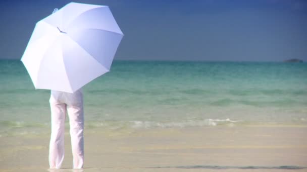 Serene jonge vrouw met een witte parasol in het ondiepe water naast een prachtige witte zandstrand — Stockvideo