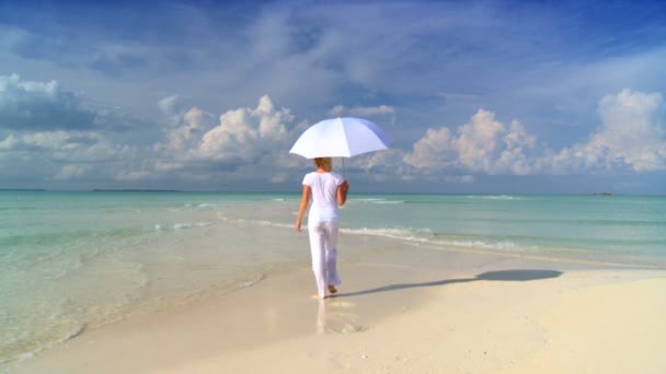 Mujer joven y serena con una sombrilla blanca en las aguas poco profundas junto a una hermosa playa de arena blanca — Vídeos de Stock