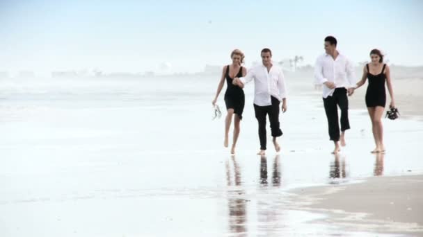 Four attractive young friends enjoying the beach early morning after a social night out — Stock Video