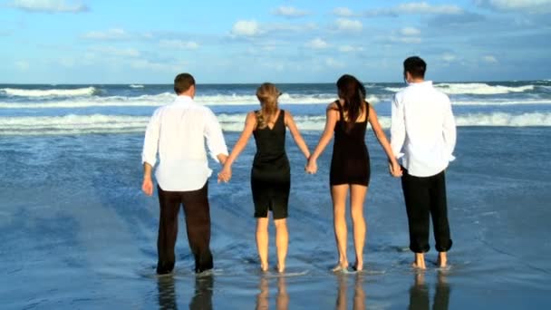 Four attractive young friends having crazy fun on the beach early morning after a social night out — Stock Video