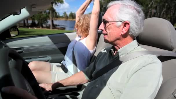 Contented retired couple enjoying driving in the sunshine in their open top car — Stock Video