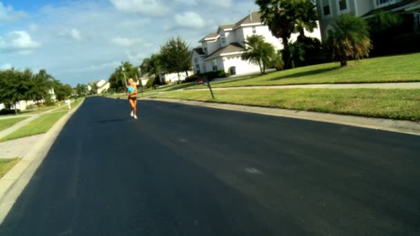 सुंदर सुनहरे बालों वाली महिला धूप में उपनगरीय सड़कों के साथ जॉगिंग का आनंद ले रही — स्टॉक वीडियो