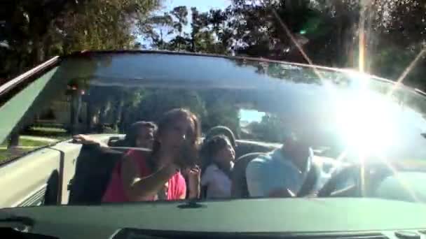 Atractiva familia caucásica disfrutando de conducir a casa bajo el sol en su coche de techo abierto — Vídeos de Stock