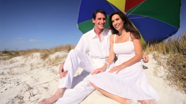 Paret sitter under stranden parasoll — Stockvideo