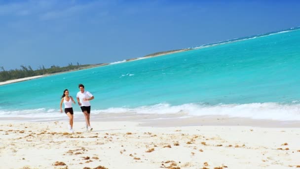 Pareja joven trotando a lo largo de la playa tropical — Vídeos de Stock