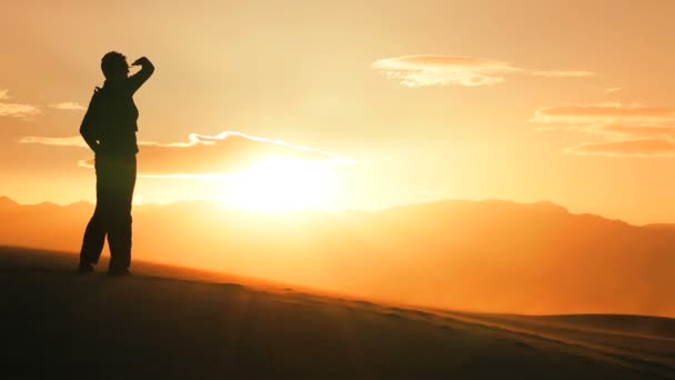 Kum tepeleri arasında hiking ve güneş ayarı izlerken siluet yalnız kadın — Stok video