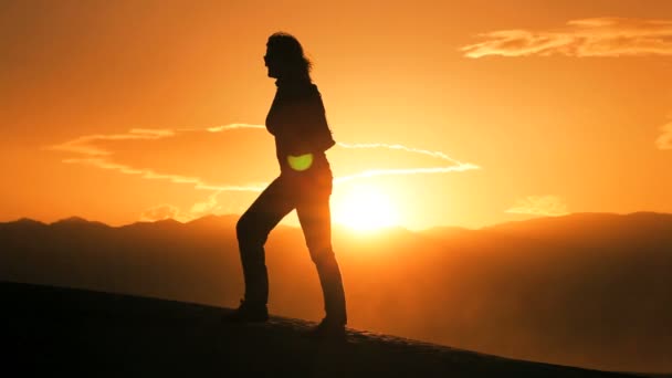 Einsames Weibchen in Silhouette wandert über Sanddünen und beobachtet den Sonnenuntergang — Stockvideo
