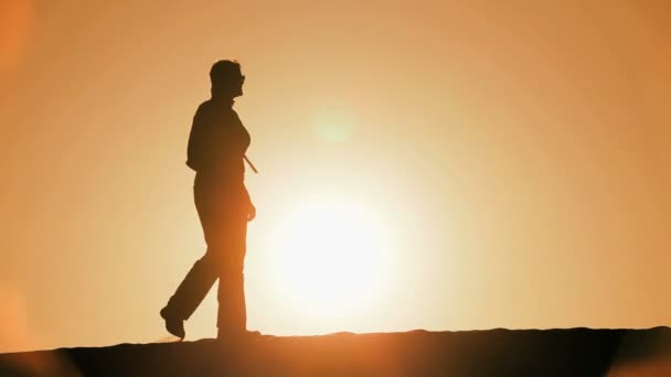 Kum tepeleri arasında hiking ve güneş ayarı izlerken siluet yalnız kadın — Stok video