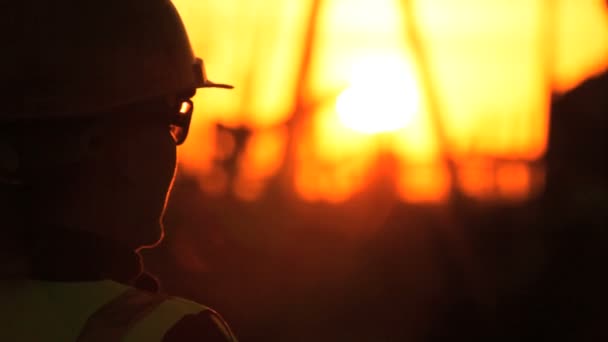 Σιλουέτα του θηλυκό μηχανικός με πρόχειρο χρησιμοποιώντας ένα κινητό τηλέφωνο που επιβλέπει την περιοχή της παραγωγής αργού πετρελαίου στο ηλιοβασίλεμα — Αρχείο Βίντεο