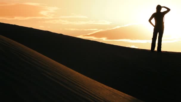 砂丘を越えてハイキング ・沈む夕日のシルエットで孤独な女性 — ストック動画