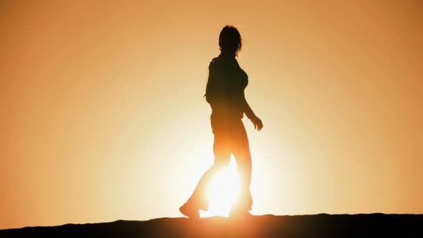 Mulher solitária em silhueta caminhando através de dunas de areia e observando o pôr do sol — Vídeo de Stock