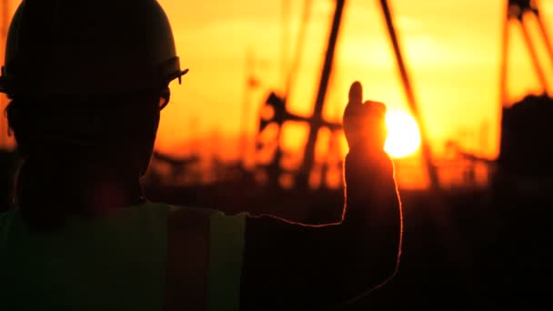 Silueta de ingeniera femenina con portapapeles utilizando un teléfono celular que supervisa el sitio de producción de petróleo crudo al atardecer — Vídeos de Stock