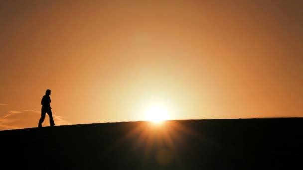 Μοναχική γυναίκα σε σιλουέτα, πεζοπορία σε αμμόλοφους & βλέποντας τον ήλιο να δύει — Αρχείο Βίντεο