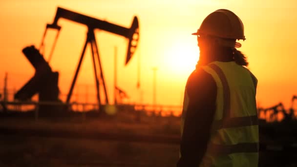 Silueta de ingeniera femenina con portapapeles utilizando un teléfono celular que supervisa el sitio de producción de petróleo crudo al atardecer — Vídeos de Stock