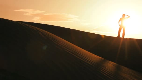 Mulher solitária em silhueta caminhando através de dunas de areia e observando o pôr do sol — Vídeo de Stock