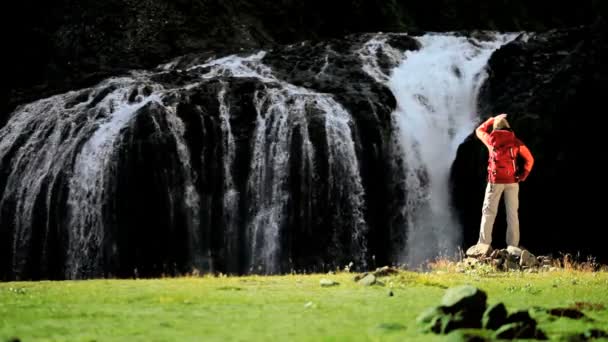 Ung vandrare som tittar på ett forsande vattenfall — Stockvideo