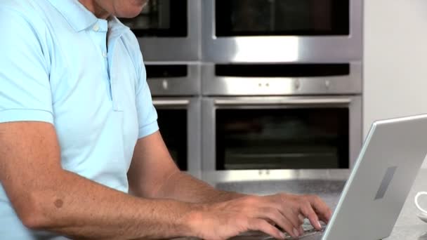 Привлекательный зрелый мужчина работает на ноутбуке на кухне — стоковое видео