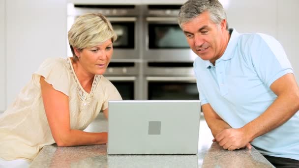 Μέσης ηλικίας καυκάσιος ζευγάρι στην κουζίνα στο σπίτι χρησιμοποιώντας φορητό υπολογιστή — Αρχείο Βίντεο