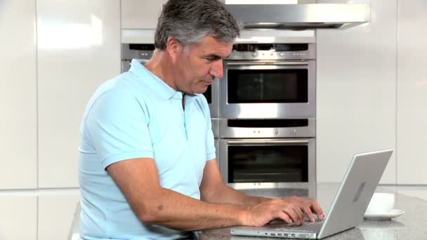 Uomo di mezza età con computer portatile sul bancone della cucina — Video Stock