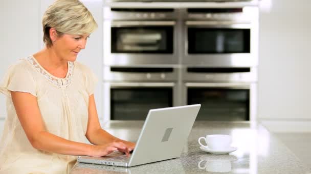 Signora di mezza età con computer portatile sul bancone della cucina — Video Stock