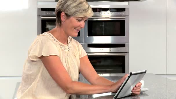 台所でワイヤレス タブレットを使用して魅力的な成熟した女性 — ストック動画