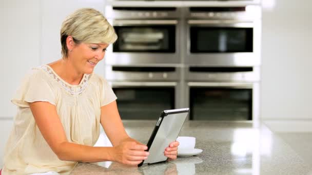 Mujer madura inteligente usando tableta inalámbrica en la cocina — Vídeo de stock