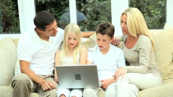 Familia joven caucásica usando el ordenador portátil en el sofá — Vídeo de stock