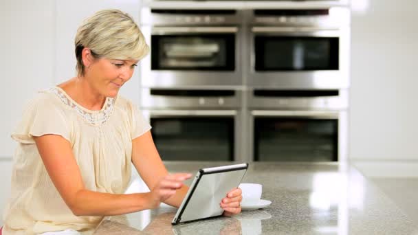 Attraktiva mogen kvinna med trådlös tablet i kök — Stockvideo