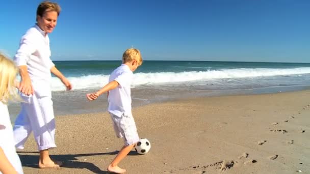 Молодая семья в погоне за мячом на пляже — стоковое видео