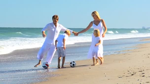 Familia joven persiguiendo una pelota en la playa — Vídeo de stock