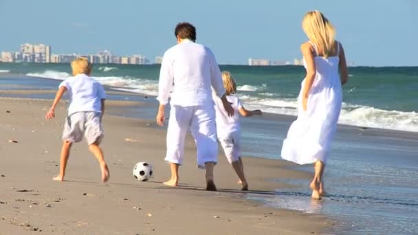 Família feliz perseguindo uma bola em uma praia — Vídeo de Stock