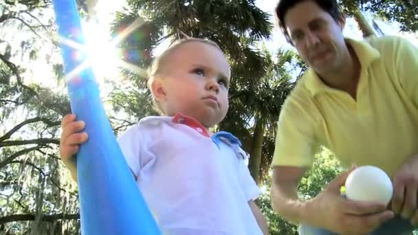 Menino feliz jogando um morcego de brinquedo na grama do parque — Vídeo de Stock