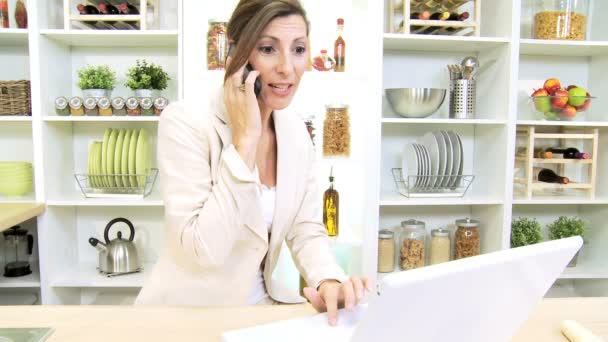 Mujer de negocios caucásica escuchar noticias y trabajar en la cocina casera usando el ordenador portátil — Vídeos de Stock