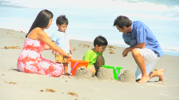 Bonitos irmãos hispânicos fazendo castelos de areia com pais — Vídeo de Stock