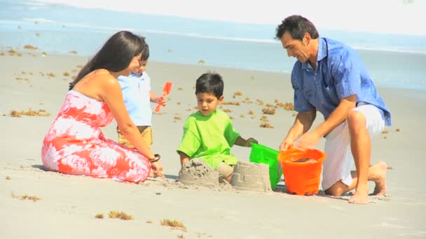 Lindos hermanos hispanos haciendo castillos de arena con padres — Vídeos de Stock