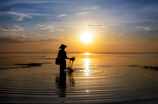 Balinese fisherman at sunrise in Silhouette fishing with nets for stock to sell in local village markets Indonesia travel tourism Asia