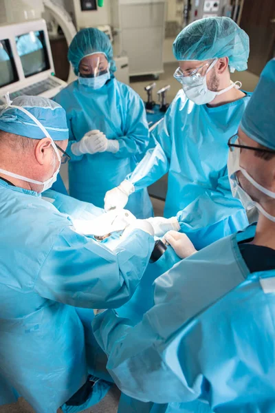 Multi ethnic surgical team wearing face masks gloves and gowns performing surgery on patient in hospital operating theatre