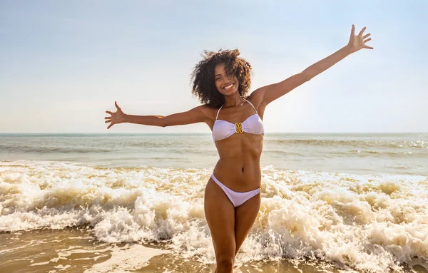 笑顔の若いアフリカ系アメリカ人女性とビーチでの海の波白いビキニを着て夏休みを楽しんで — ストック写真