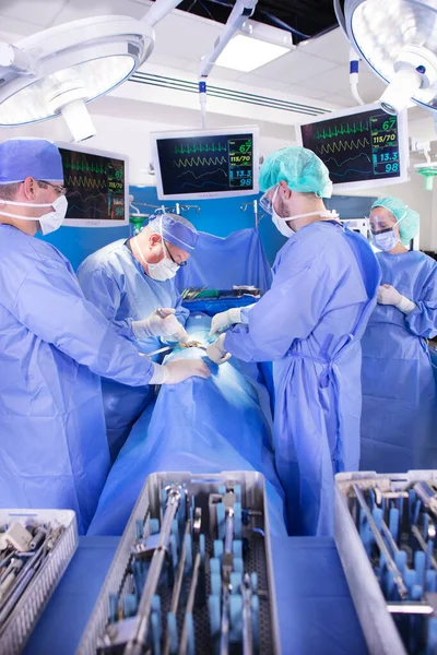 Medical team wearing scrubs in hospital operating theatre performing surgery on patient using sterile instruments and monitors